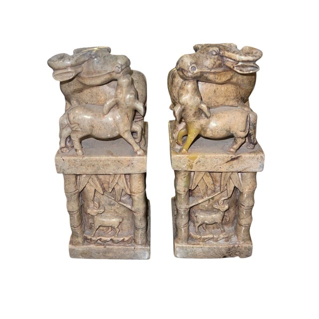 A finely carved pair of Chinese soapstone sculptures depicting water buffalo with calves, raised on square architectural...