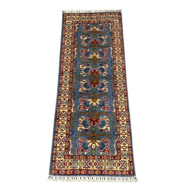 This blue wool runner features a repeating stylized floral pattern in cream, burgundy, rust, and gold. Layered patterned...