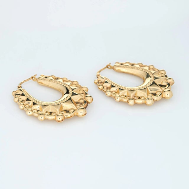 Fine detailed pair of oval hoop earrings crafted in 14k yellow gold. The stylish earrings feature an elaborate scrolled...