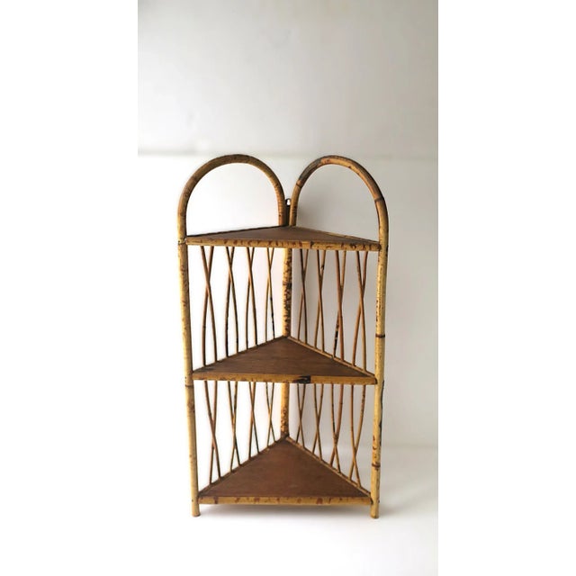 A wicker bamboo corner wall or floor shelf etagere. Piece has three (3) storage shelves with crisscross latticework style...