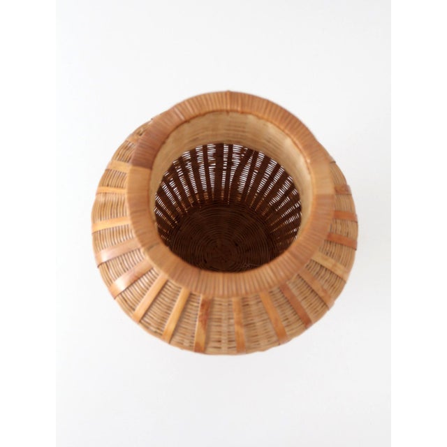 A vintage wicker vase featuring a sculptural basket-form silhouette and finely woven reed construction. The rounded body,...