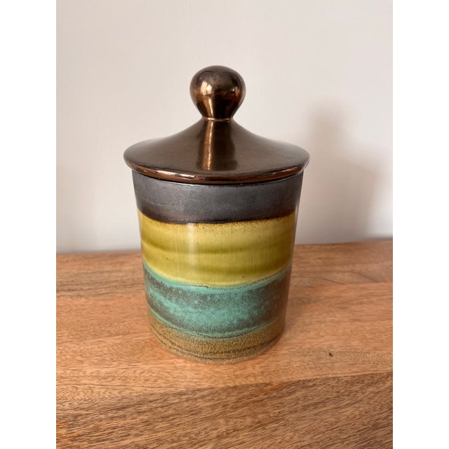 A stunning piece from celebrated Ecuadorian artist, Eduardo Vega. This banded beauty features a metallic bronze glazed lid...