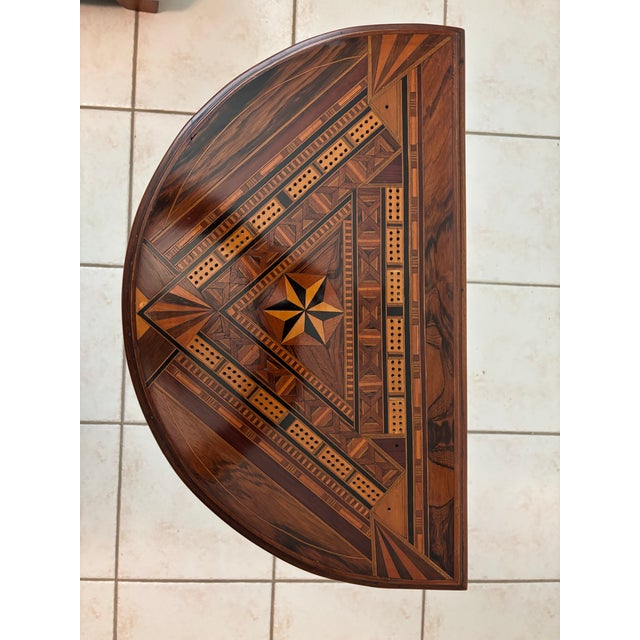 A beautifully crafted three‑leg demi‑lune game table featuring an intricate marquetry inlaid top with geometric motifs and...