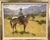 The painting depicts a cowboy in a straw hat riding a gray horse through a mountainous desert landscape. Anton's work has...
