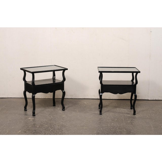 A French pair of black two-tiered end tables, with single drawer, from the mid 20th century. These mid-century end tables...