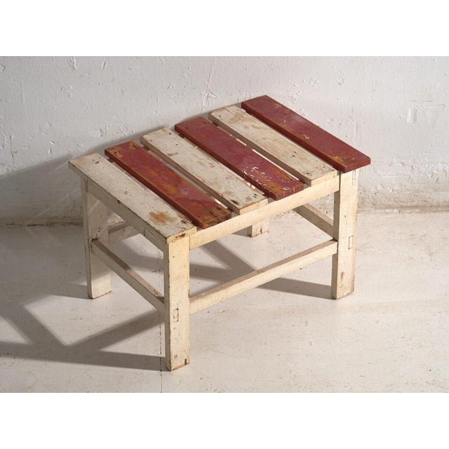 This antique rustic low bench in wood is a low seat with a slatted top and a stretchered frame, of rectangular plan. It...