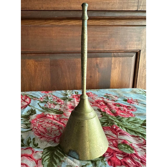 Vintage brass bell that has a conical shape with a long, slender handle. Measures 7” tall.