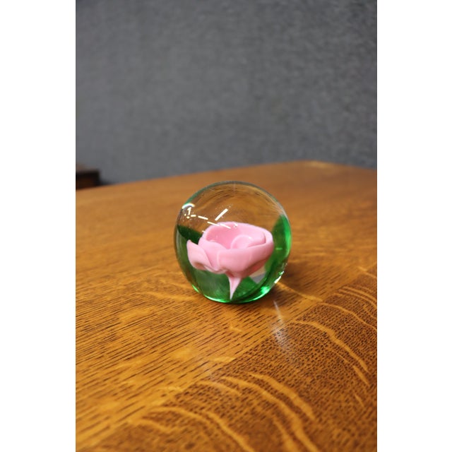 Hand-blown art glass paperweight featuring a pink rose encased in clear glass with green accents. Dated 1980 on the...