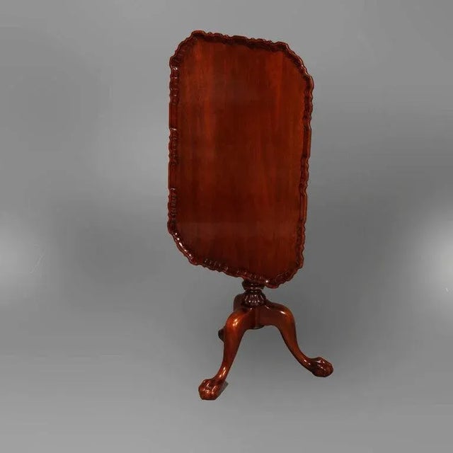 An antique Chippendale style tea table offers mahogany construction with clip corner tilt-top having ruffled rim and...