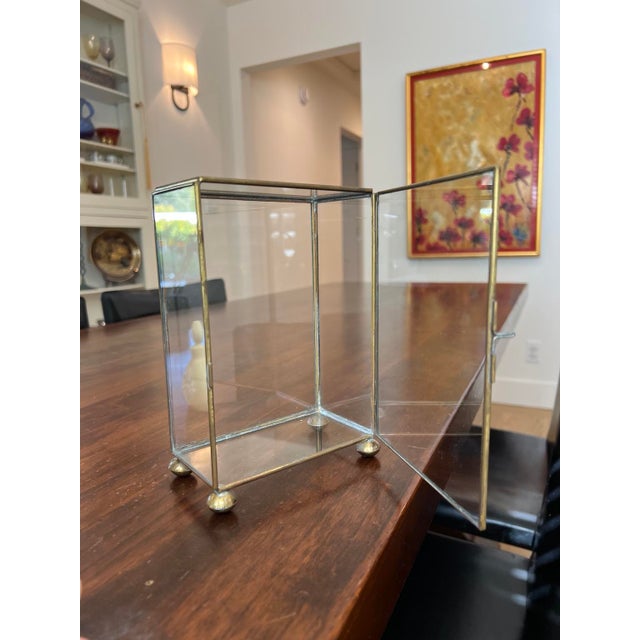 Vintage brass and glass tabletop display case with a hinged front door, small latch and brass ball feet. Glass panels on...