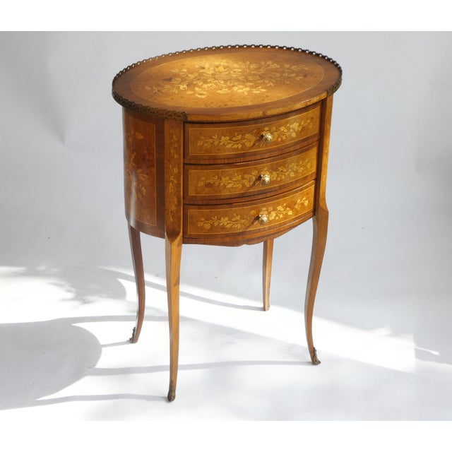 An amazing large oval French Louis XV style nightstand with three drawers. The wooden table has beautiful floral inlaid...