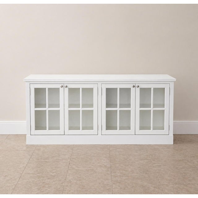A beautifully scaled 72-inch white painted sideboard featuring four paneled glass doors and a clean, architectural...