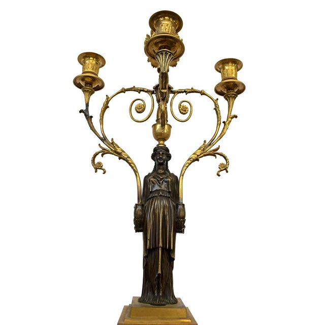 A pair of antique French candelabras made of burnished bronze and gilded brass. They feature female figures on square...