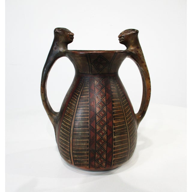 A vintage pre- Colombian styled painted terracotta pottery vase with geometric patterns and handles having the body and...
