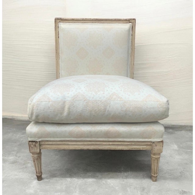 An antique Louis XVI style upholstered slipper chair with a distressed wooden frame and fluted legs. Originally developed...