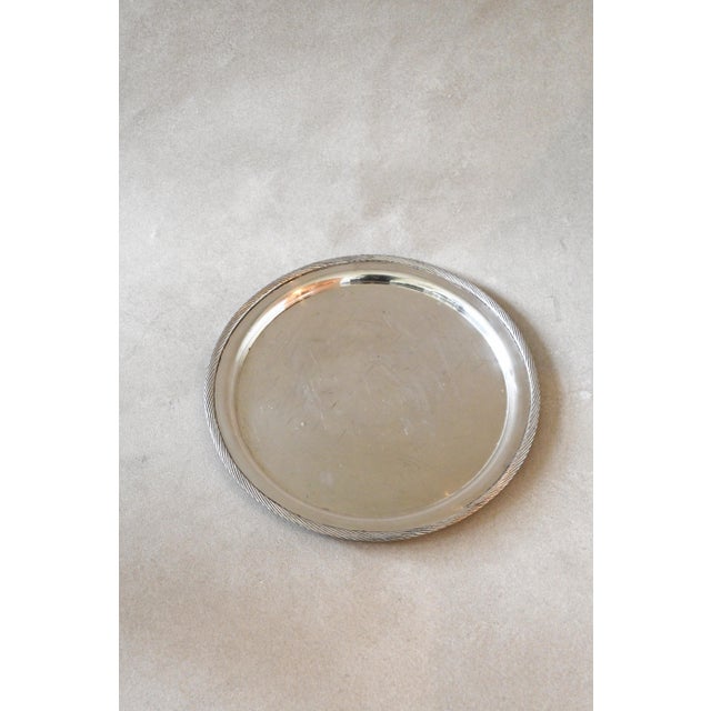 A large round silverplate tray framed by a twisted rope border, with a plain center that shows a soft, lived-in patina....