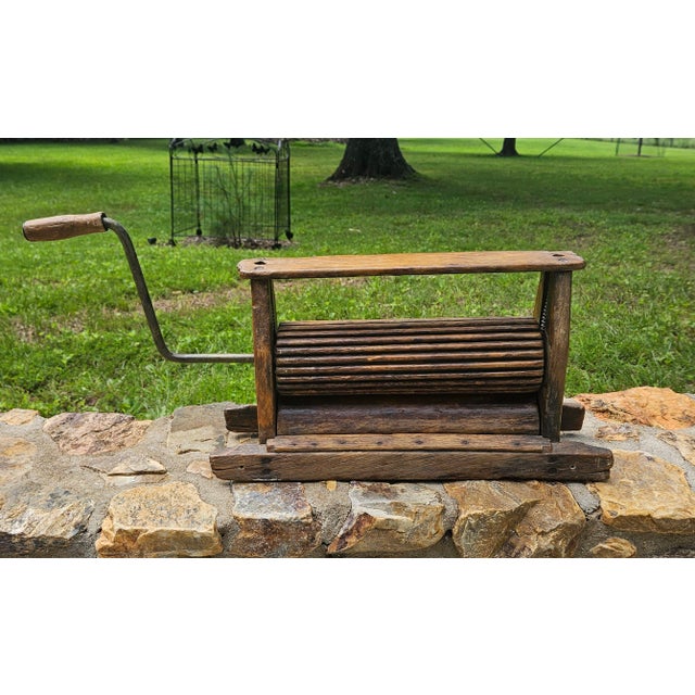 A vintage wooden clothes wringer, historically used for removing water from laundry, operates with a hand-cranked press...
