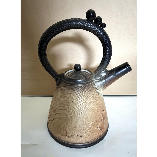 A sculptural studio teapot by American potter Mark Untener, c. 1990s–2000s. The conical tan stoneware body is carved with...