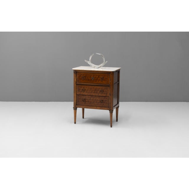 Marble top three drawer commode with leathered pull out. Inlaid parquetry drawer fronts and original brass mounts and...