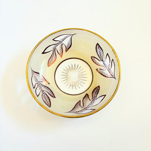 A mid century glass bowl decorated in a white and metallic gold leaf design. Measures 6.25"Dia x 1.75"H