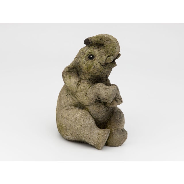 An English late-20th-century composite stone garden statue depicting a seated elephant with rounded, stylized features and...