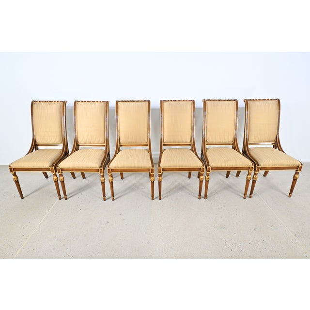 An elegant set of six neoclassical-style dining side chairs crafted in richly grained wood with refined gilt accents. The...