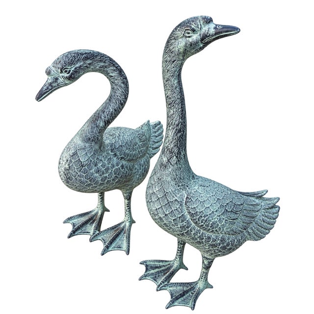 A striking pair of life-size cast metal geese sculptures with beautifully detailed feathering and a rich green verdigris...