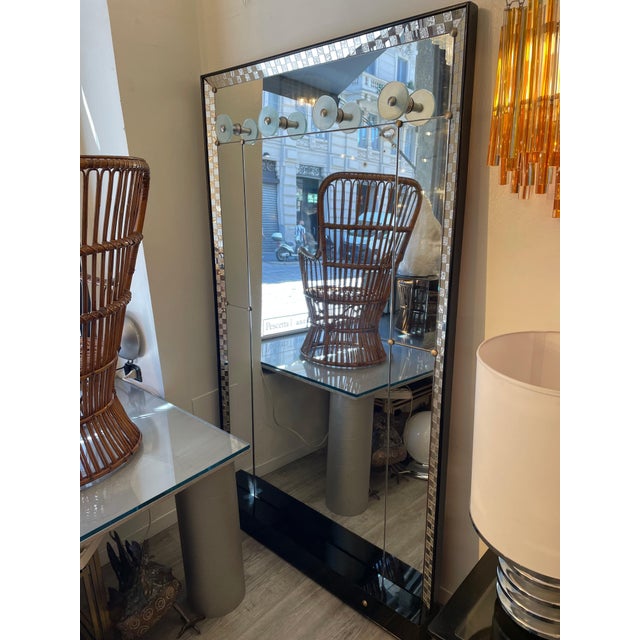 A 1970s entryway mirror unit with a built-in coat rack. The mirror is framed by a mosaic of mirror tiles and screen-...