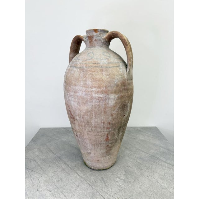 An antique amphora from the Puglia region with an elegant elongated shape and unglazed surface highlighting its hand-...