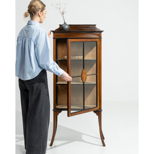 A delicate Edwardian cabinet featuring fine inlay work and elegant proportions. The decorative marquetry highlights...