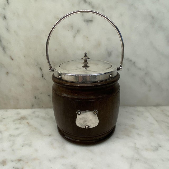 English oak biscuit barrel which retains its original porcelain liner and is decorated with a silverplate crest. DETAILS...