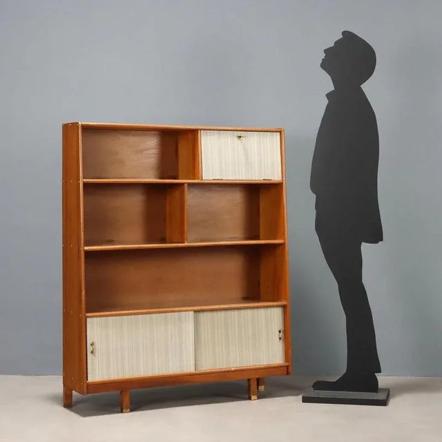 Vintage wooden bookcase with shelves and open compartments, sliding and flap doors. This piece is attributed to the...