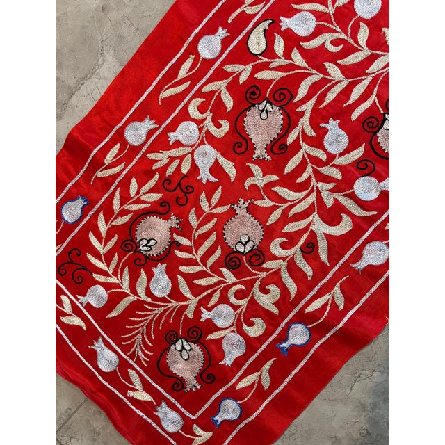 Hand-embroidered Suzani table runner from Uzbekistan — cream and ecru vine scrolls with pomegranate buds on a deep red...