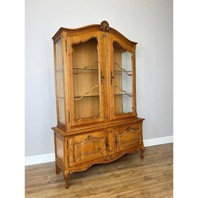 An elegant Vintage French Louis oak bookcase featuring a glazed upper display section, decorative shaped detailing and a...