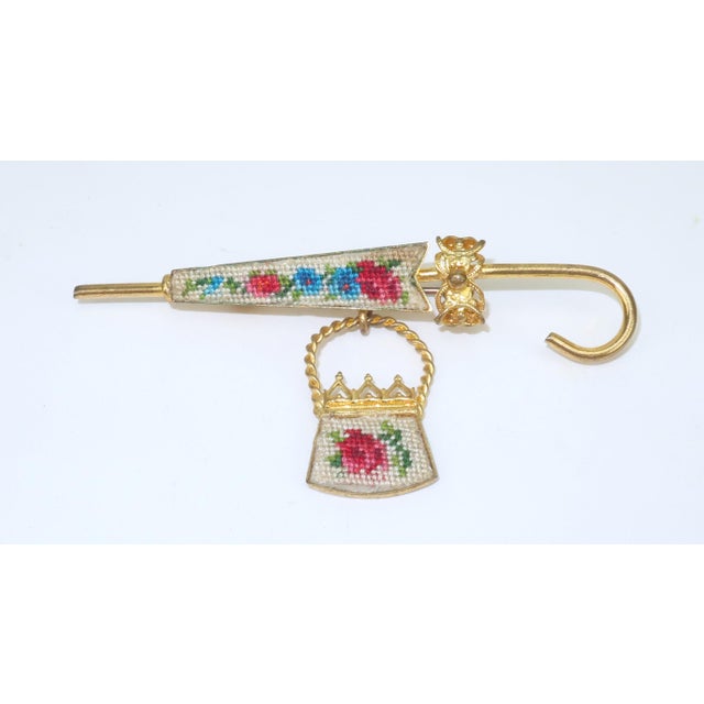 Charming parasol and purse brooch in a gold tone metal embellished with a floral petit point in shades of red, pink, blue...