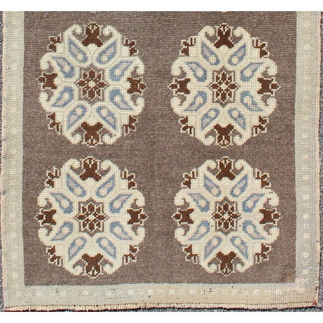 This Turkish Oushak gallery rug features ten floral medallions that take center stage on a brown field. The border reveals...