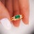 Dainty and slim, a 14K yellow gold ring featuring a vivid deep green emerald in a classic 2 row open gap setting with...