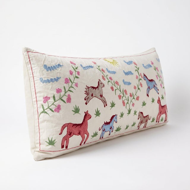 An extra-long lumbar pillow cover made from hand-embroidered Uzbek Suzani cotton — pink and blue horses among embroidered...