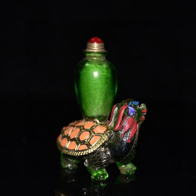This striking snuff bottle is crafted from vibrant green glass, featuring a unique and intricate design. The base is...