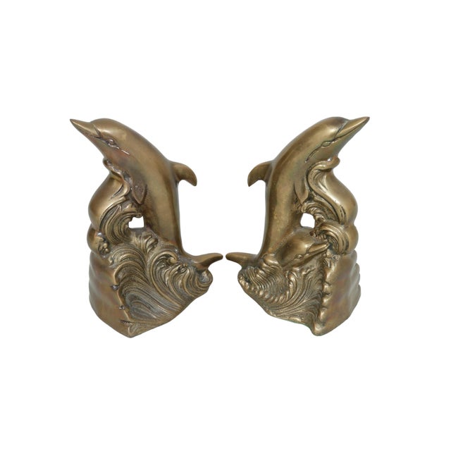 A pair of brass bookends made by Andrea by Sadek. Each is cast in the shape of a dolphin with calf breaching a scrolling...