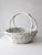 A vintage white-painted wicker basket featuring an oval form, shallow woven body, and twin arched handles that meet at the...