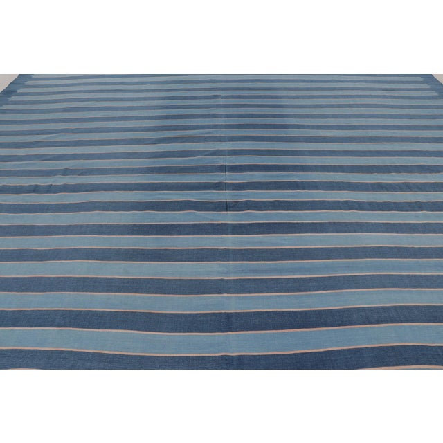 This monumental 14x15 oversized Dhurrie rug features horizontal stripes in deep indigo and soft blue, representing an...