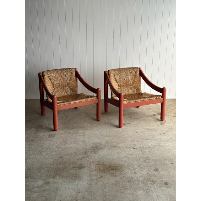 Pair of sculptural lounge chairs in a red lacquered finish with cylindrical legs, softly curved arms, and woven rush seats...