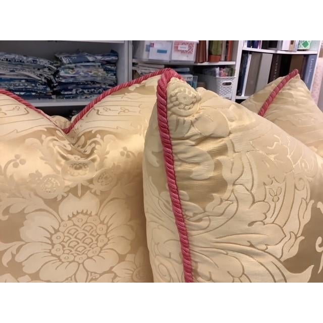 Pair of 22" x 22" down filled pillows in golden yellow damask Brunschwig & Fils fabric with coral pink rope trim.