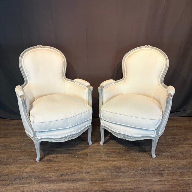Pair of French Louis XV bergère chairs, distinguished by delicately carved floral and foliate motifs along the apron,...