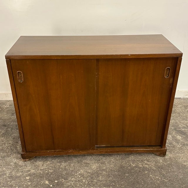 Mid Century John Widdicomb walnut sideboard or storage chest with sliding doors. The sliding doors feature recessed oval-...