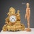 Parisian clock in gilded antimony with plant motifs. The clock is surmounted by a female figure and a cherub within a...