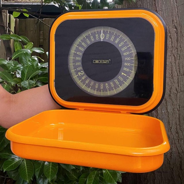 Orange wall mounting EKS kitchen scale by EKS of Sweden. The scale weighs up to 3 kilograms with 25 gram increments. The...