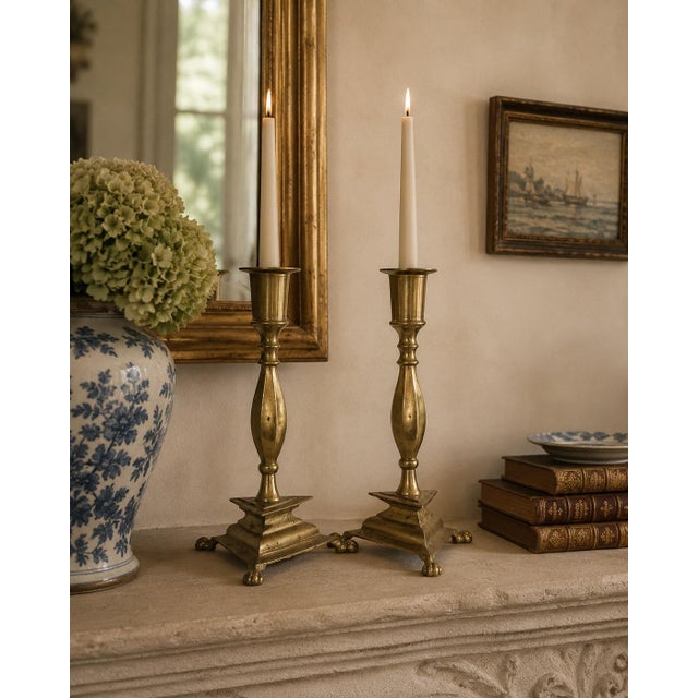 A handsome pair of mid-20th century brass candlesticks with faceted stems, stepped geometric bases, and finely modeled paw...