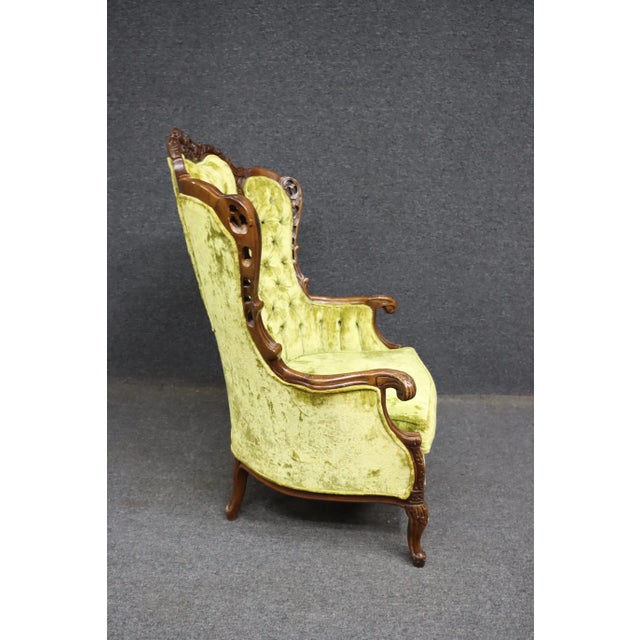 French wingback chair with carved frame and tufted back upholstered in green crushed velvet.